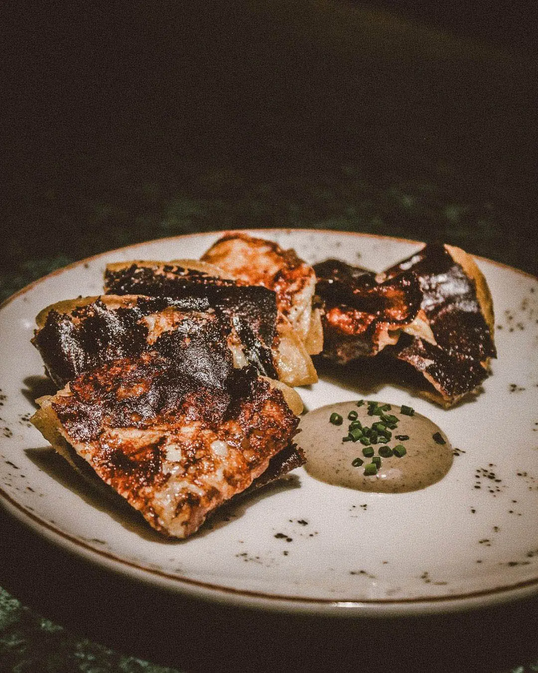 Charred flatbread pizza on a plate with a dipping sauce and herb garnish